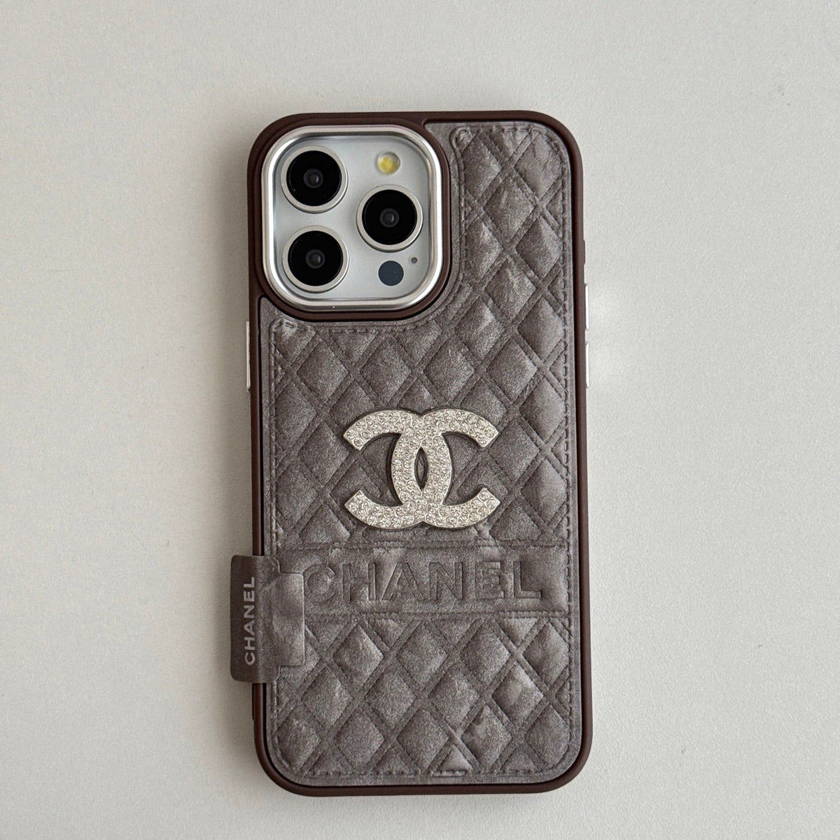 Taupe quilted iPhone case with a silver-tone emblem and side grip tab