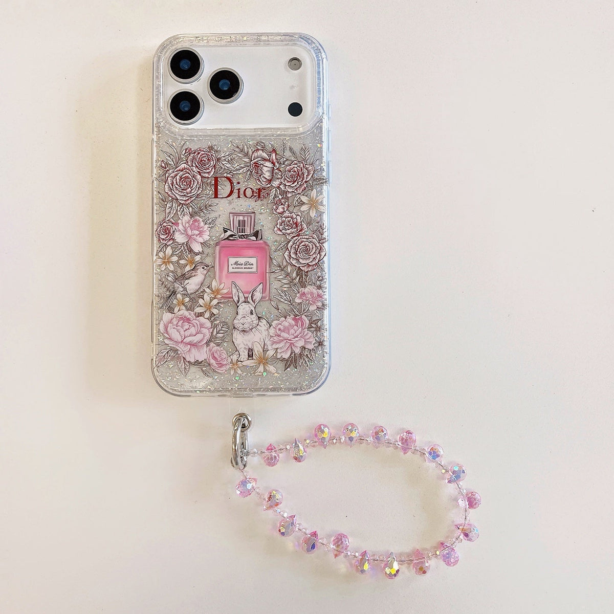 Clear pink floral iPhone case with a perfume graphic and beaded wrist strap