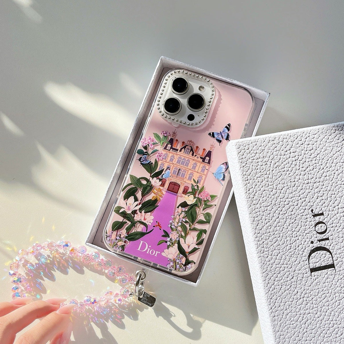Pink illustrated iPhone case with floral scenery and a beaded wrist strap