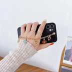 Black LV ornament iPhone case shown in a lifestyle view with the wrist strap attached