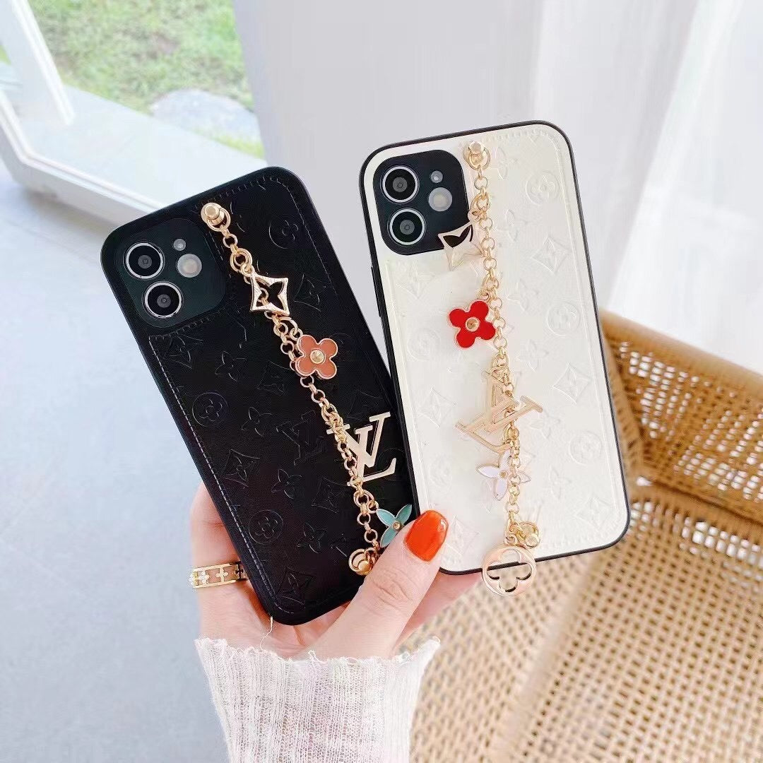 White LV ornament iPhone case shown in hand with the decorative wrist strap and leather back